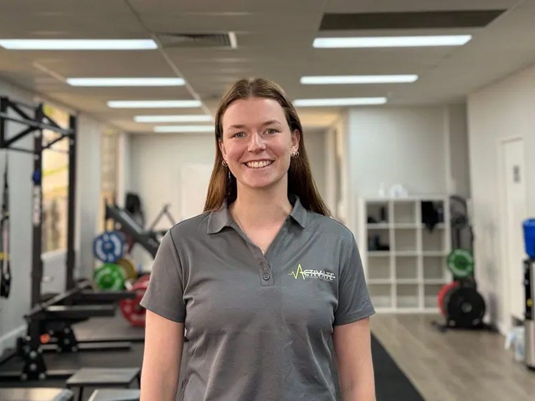 Smiling person in a gray polo standing in a gym with exercise equipment in the background