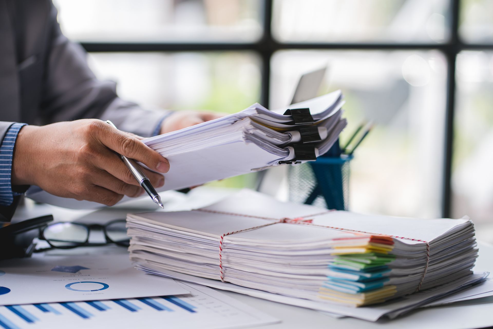 Hands sorting stacks of paperwork with colorful tabs on an office desk