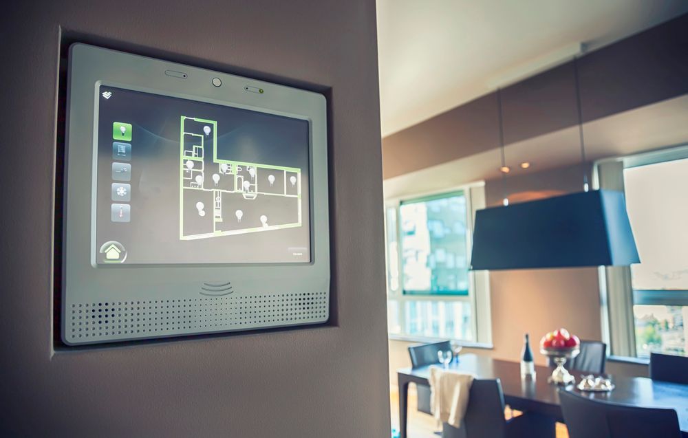 Pannello di controllo bianco per la casa intelligente incassato nella parete, che mostra la planimetria. Sala da pranzo sullo sfondo.