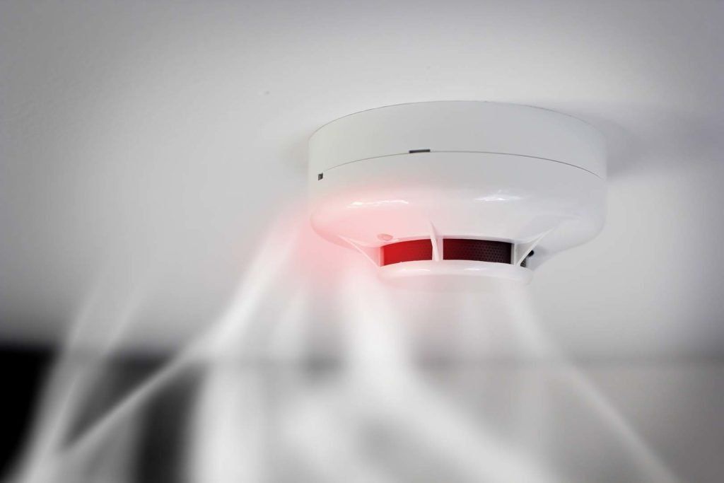 Rilevatore di fumo bianco sul soffitto, che emette luce rossa con fumo circostante.