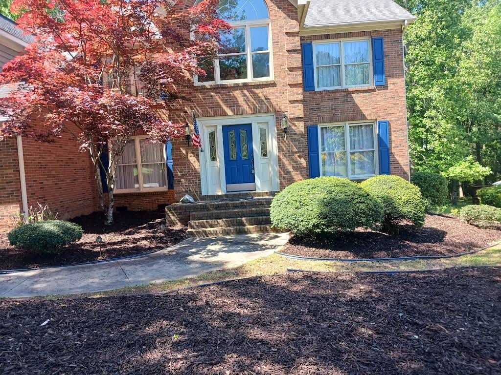 Two-story brick house with a blue front door, white trim, and a large red maple tree in the front yard.