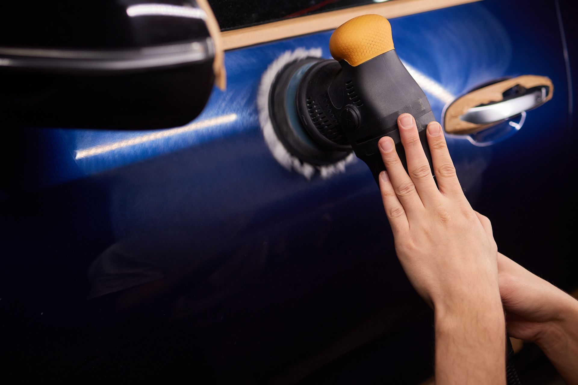 Hands polishing a blue car door with a sponge and cloth near the handle