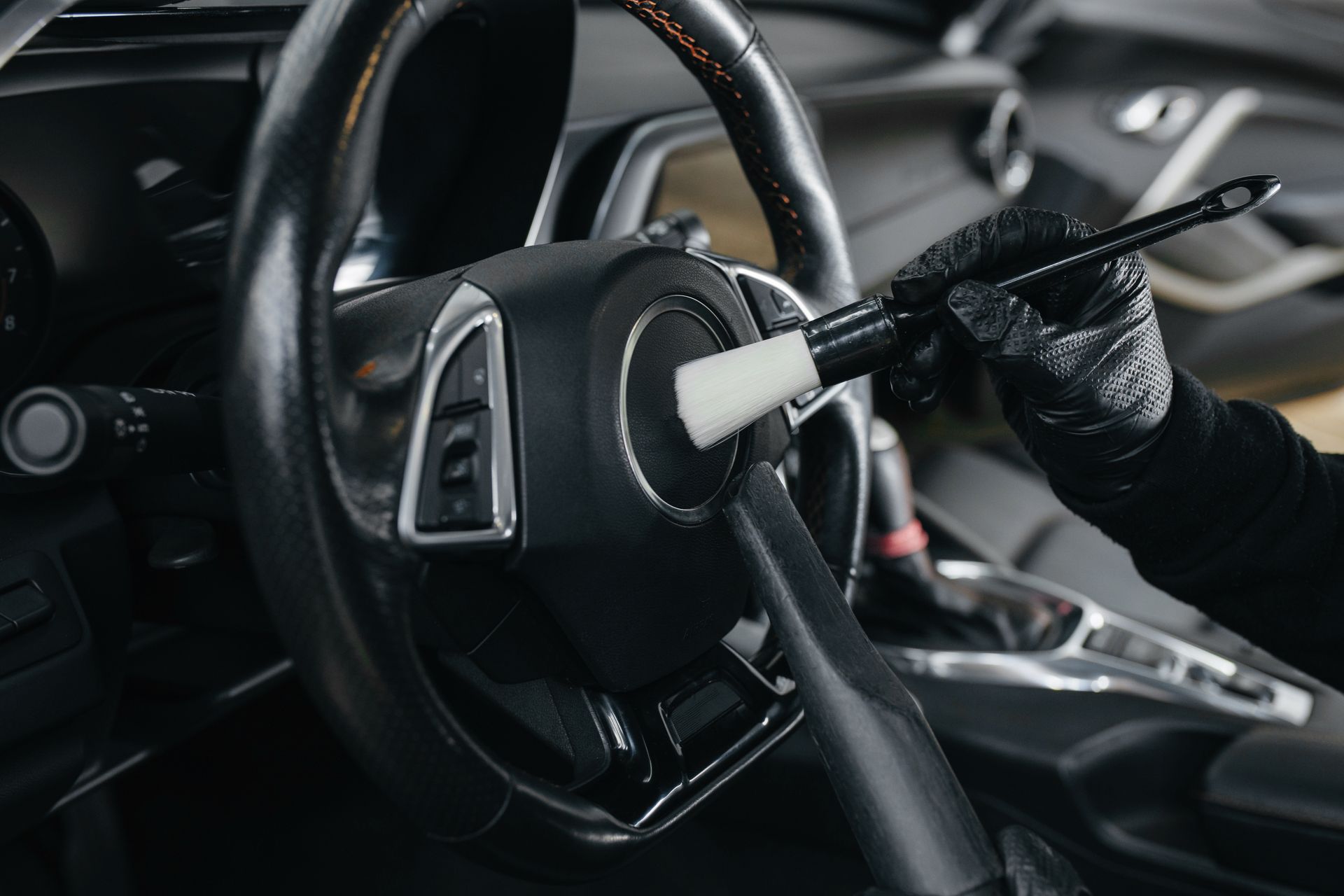 Close-up of a car steering wheel and gear shifter with a gloved hand in the driver’s seat
