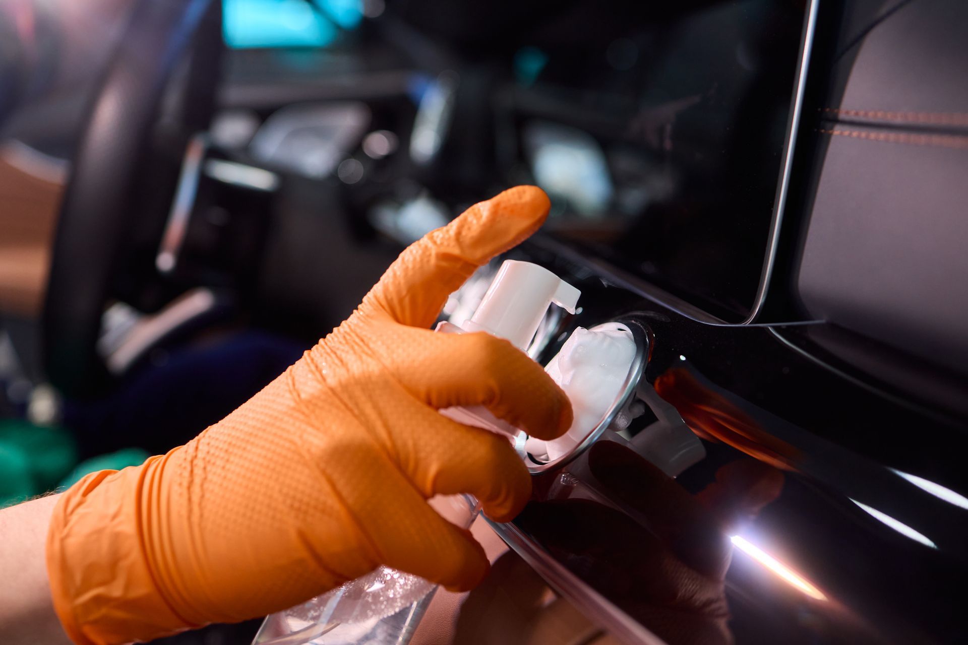Orange-gloved hand polishing a black car’s exterior near the rear light