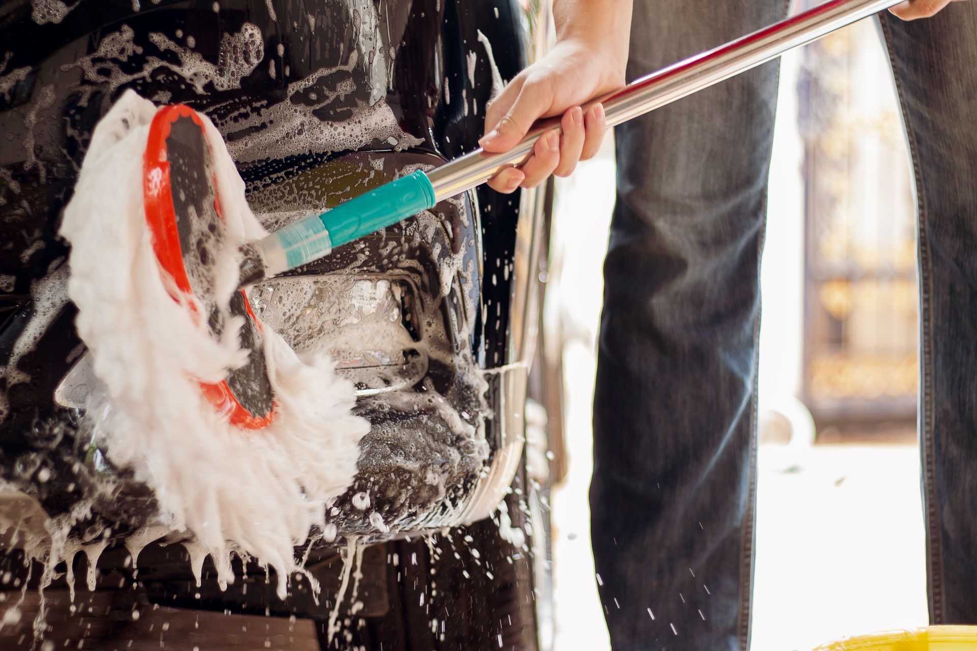 Person scrubbing a black surface with a red and green brush, covered in soap suds