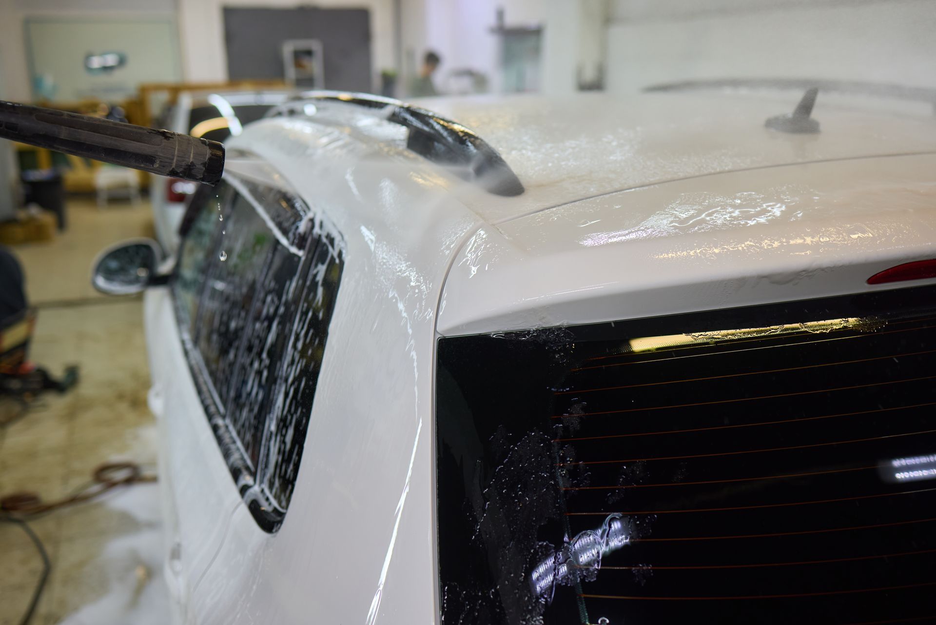 Close-up of a white car being wrapped with transparent film in a garage