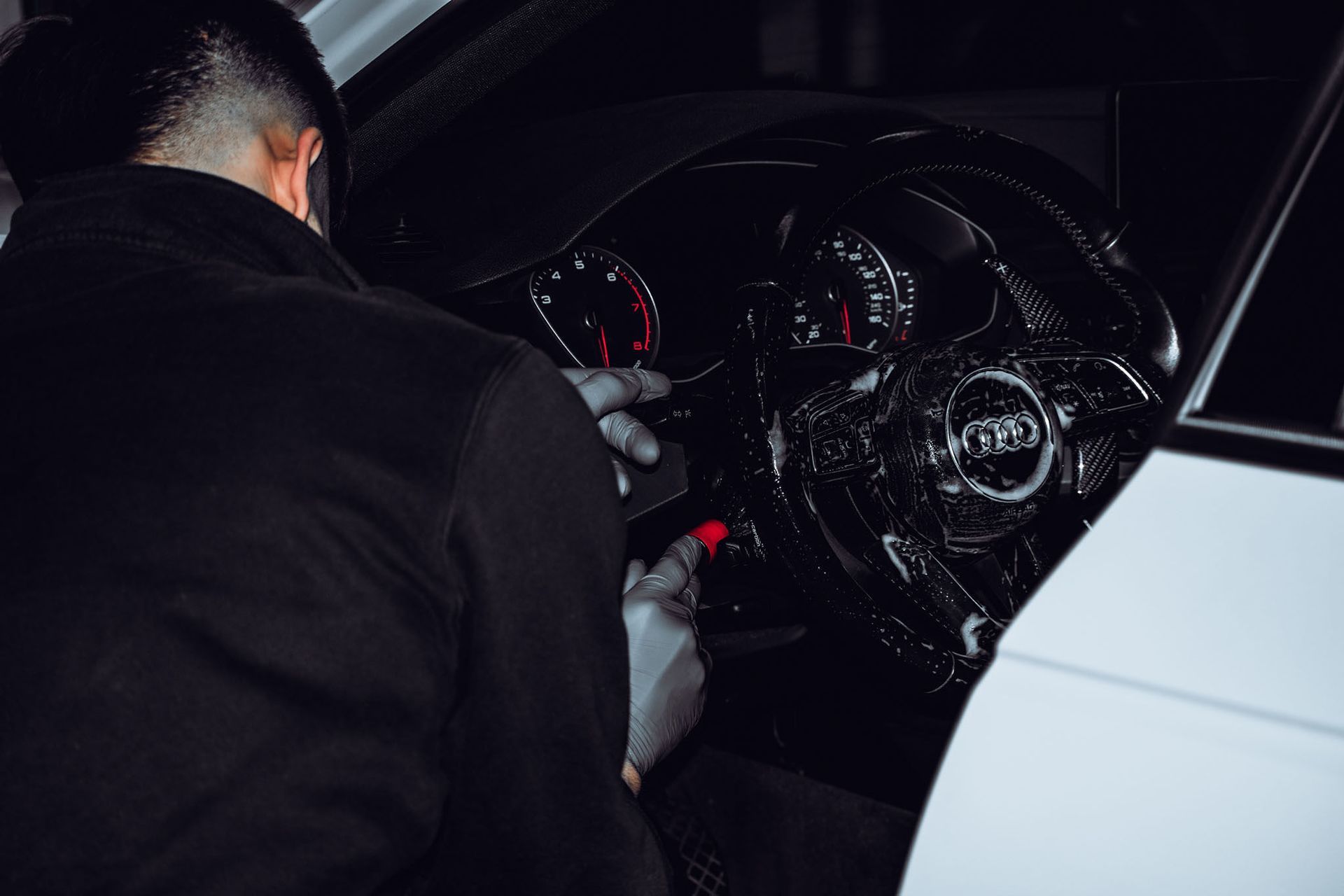 Person inspecting a car’s dashboard at night, with illuminated gauges and a white vehicle door visible.