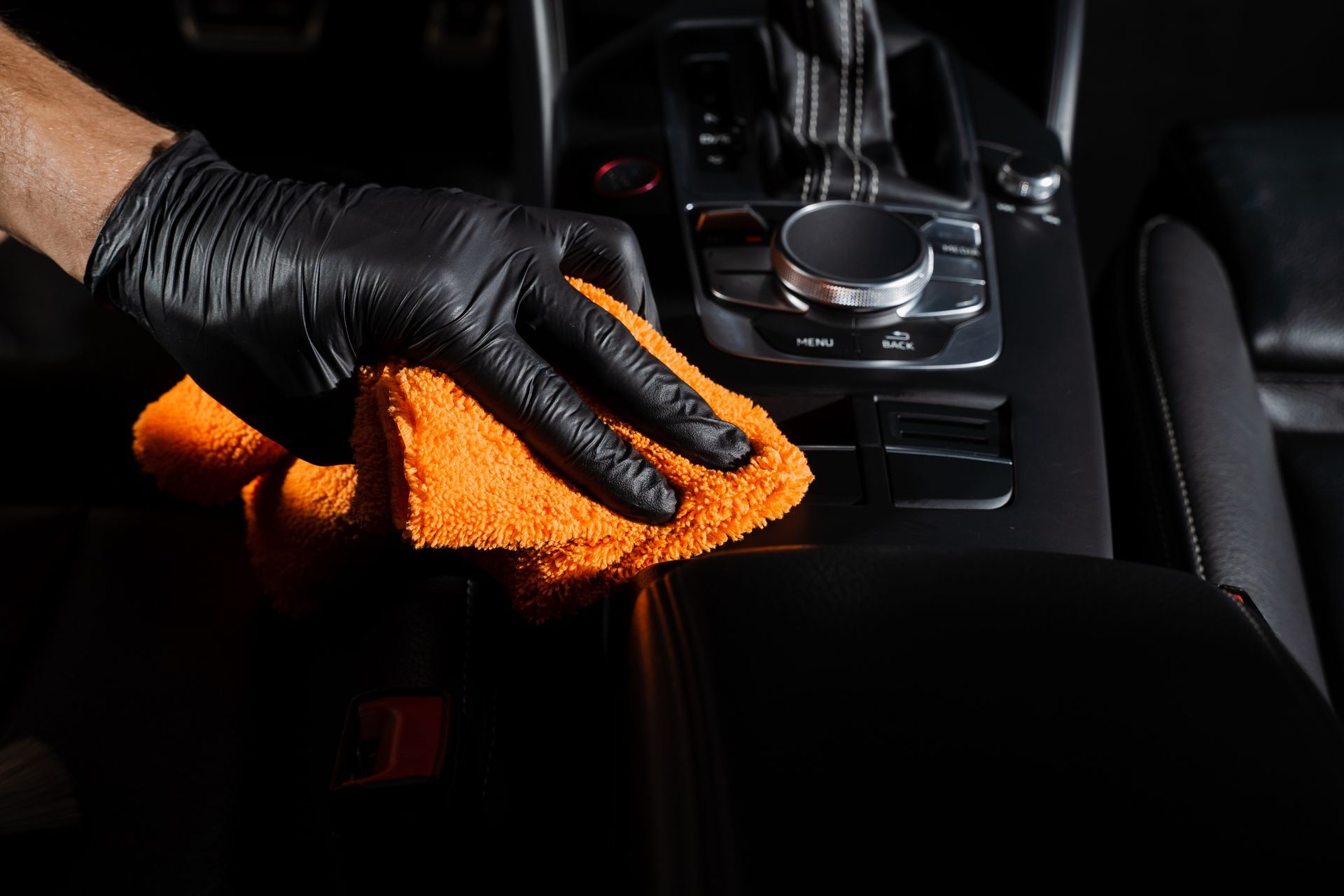 Black-gloved hand wiping a car’s center console with an orange cloth
