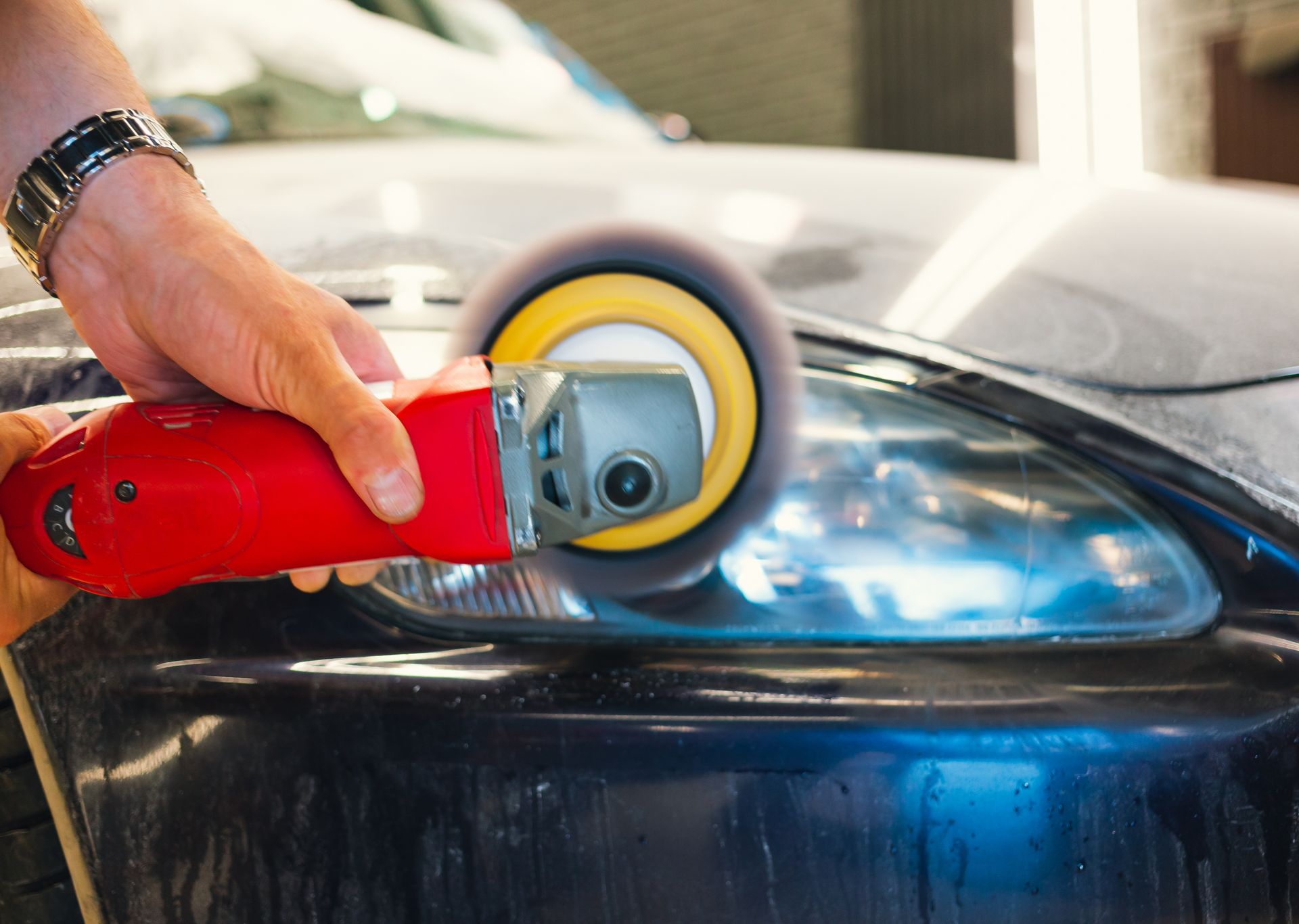 Hand polishing a black car headlight with a red orbital buffer