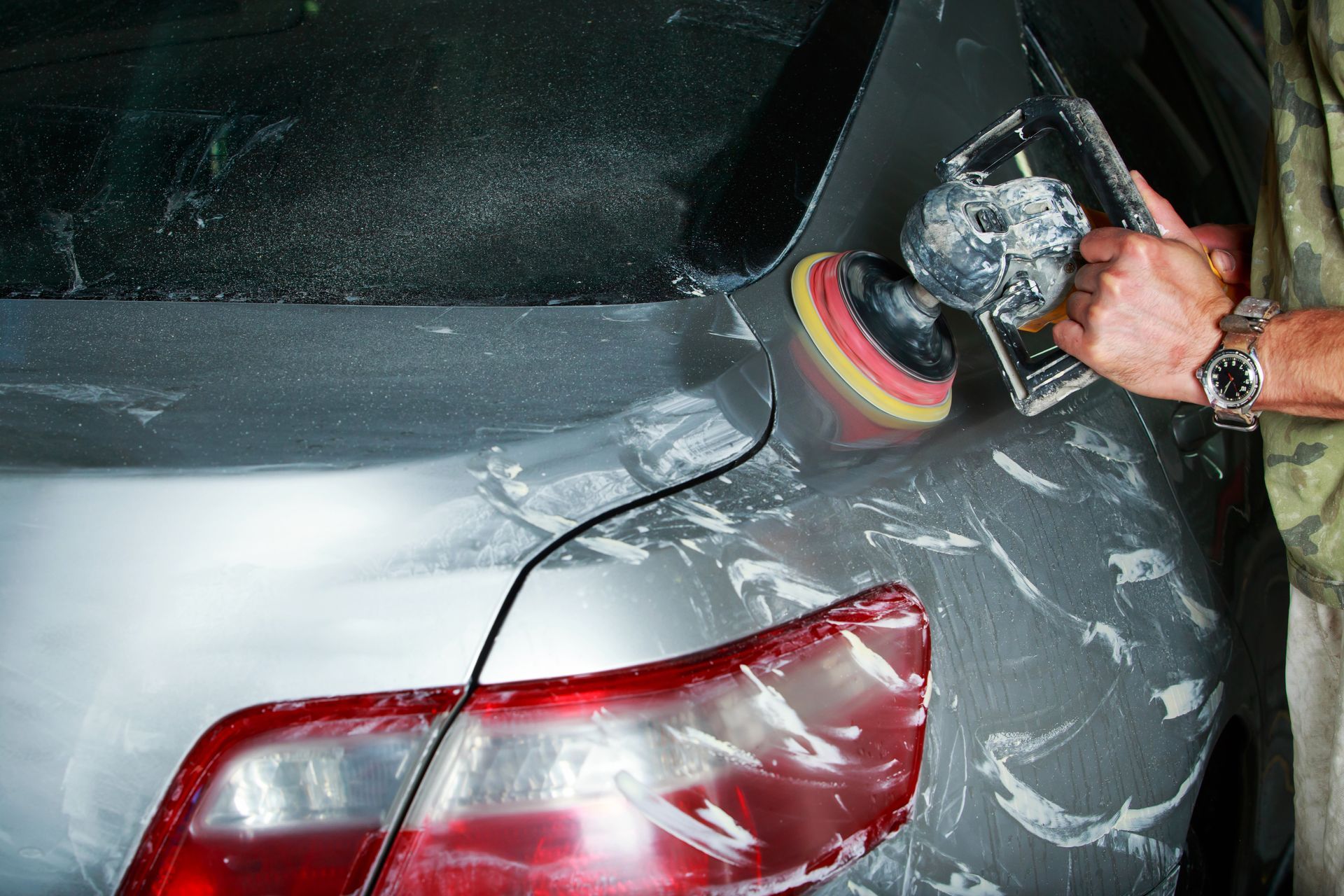 Person polishing a gray car’s rear quarter panel with a buffer, leaving white polish residue.