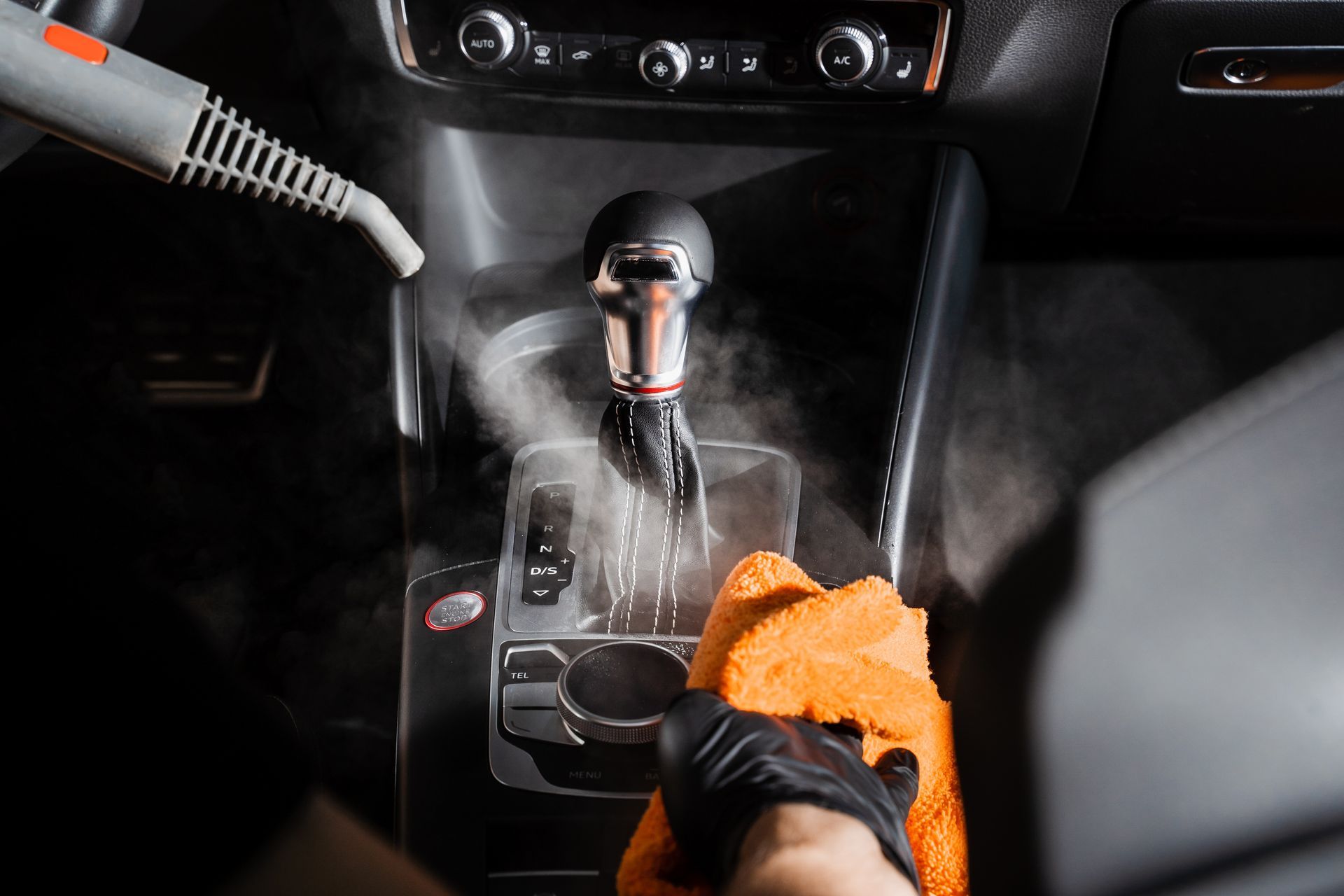 Person cleaning a car’s center console with an orange cloth and steam cleaner