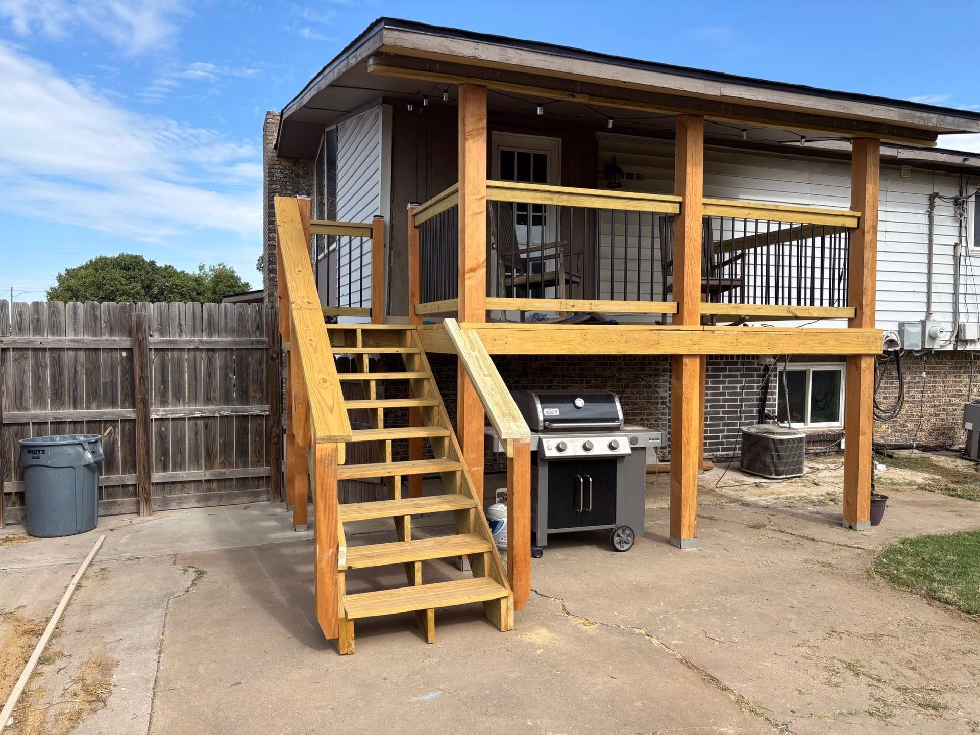 Wooden backyard deck with stairs, railing, and a grill under the platform beside a fenced yard.
