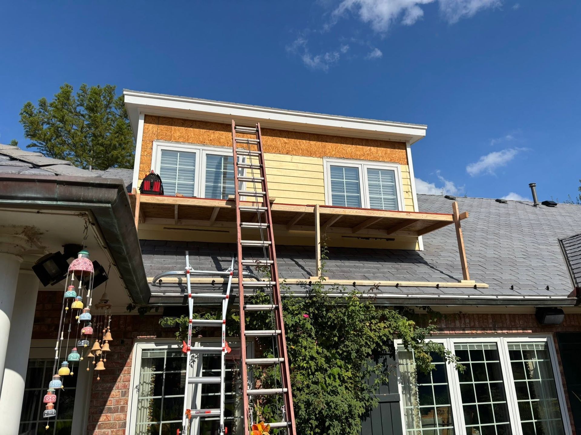 Two ladders against a house under renovation, with an unfinished second-story addition and blue sky.
