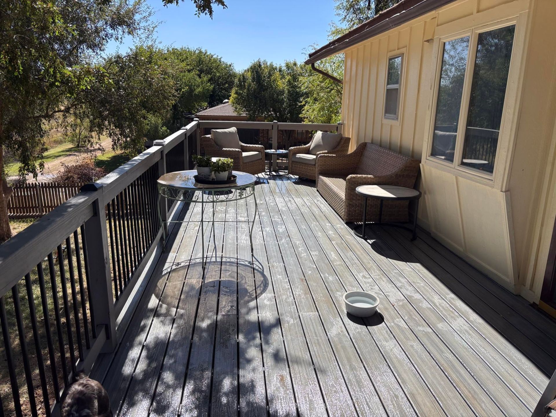 Sunny wooden deck with wicker chairs, railing, and a beige house wall with windows