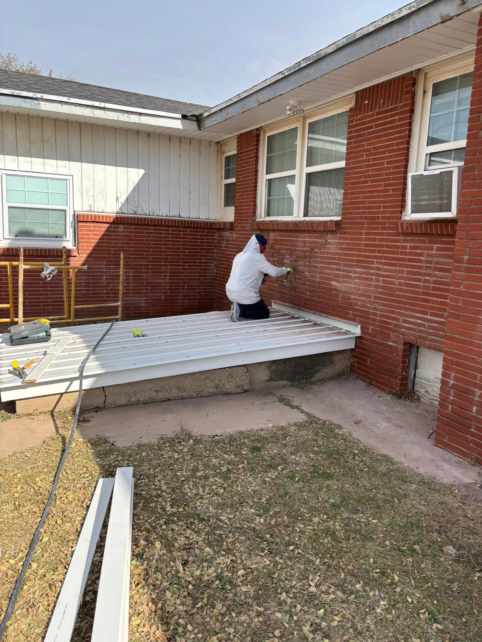 Person kneels on a new white patio beside a red brick house, working near the wall.