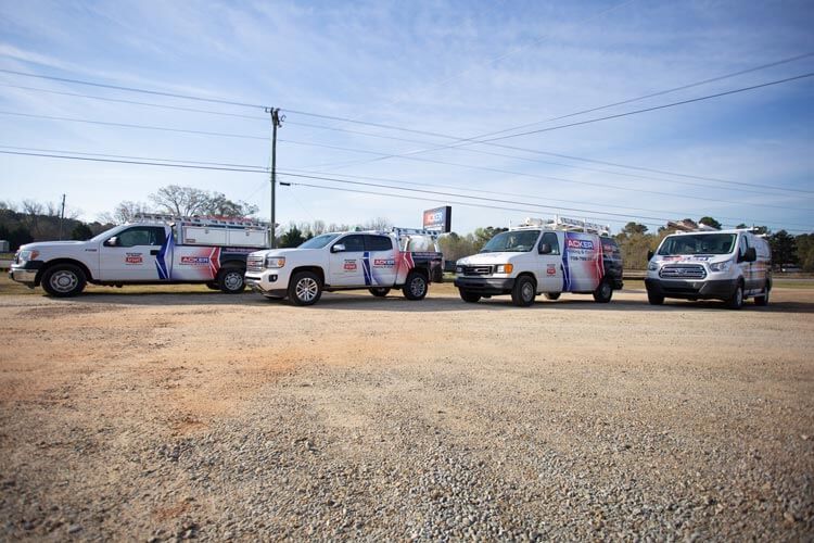 Four white service trucks parked in a gravel lot under a cloudy sky.