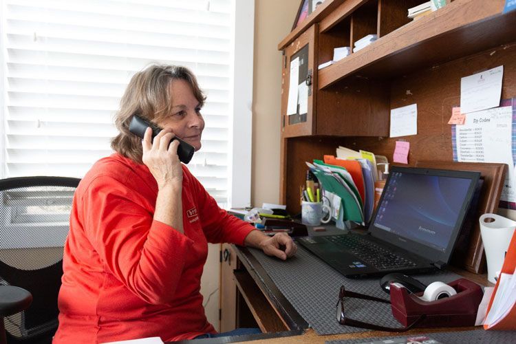 Woman in red sweater using a phone at a desk with a laptop and office supplies