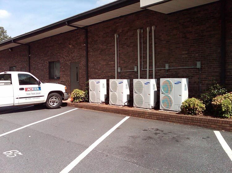 Parking lot with a white service truck and several outdoor HVAC units against a brick wall