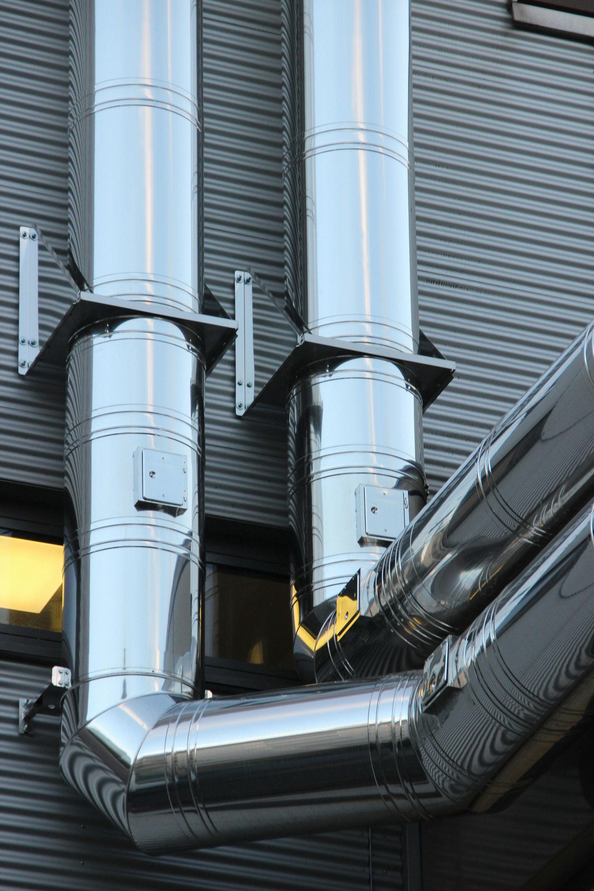 Silver rooftop ventilation ducts against a corrugated metal building wall