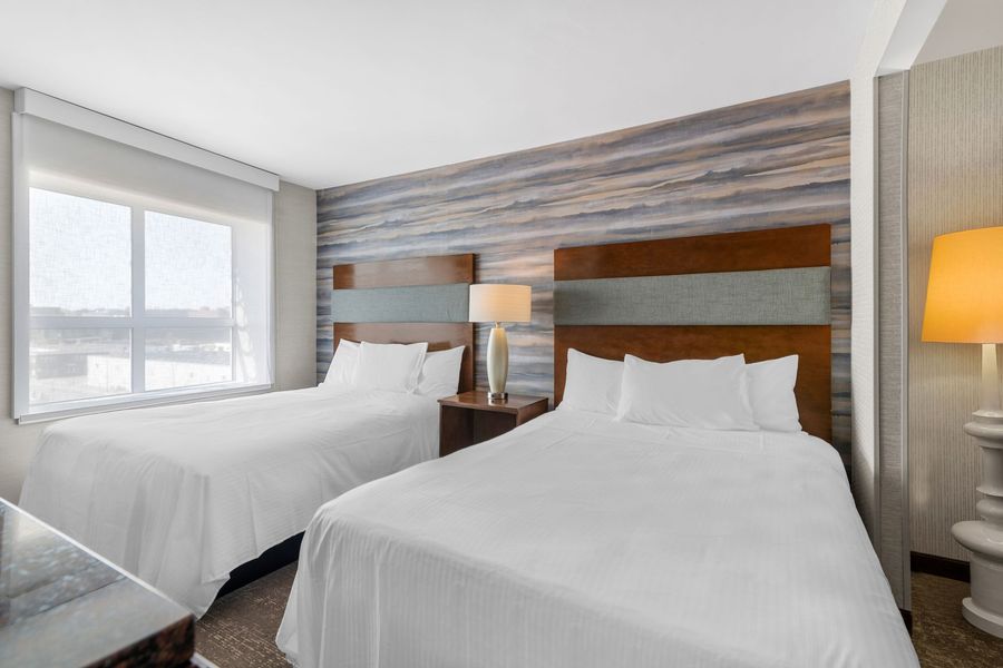 Modern hotel room with two white beds, wood headboards, and a window view