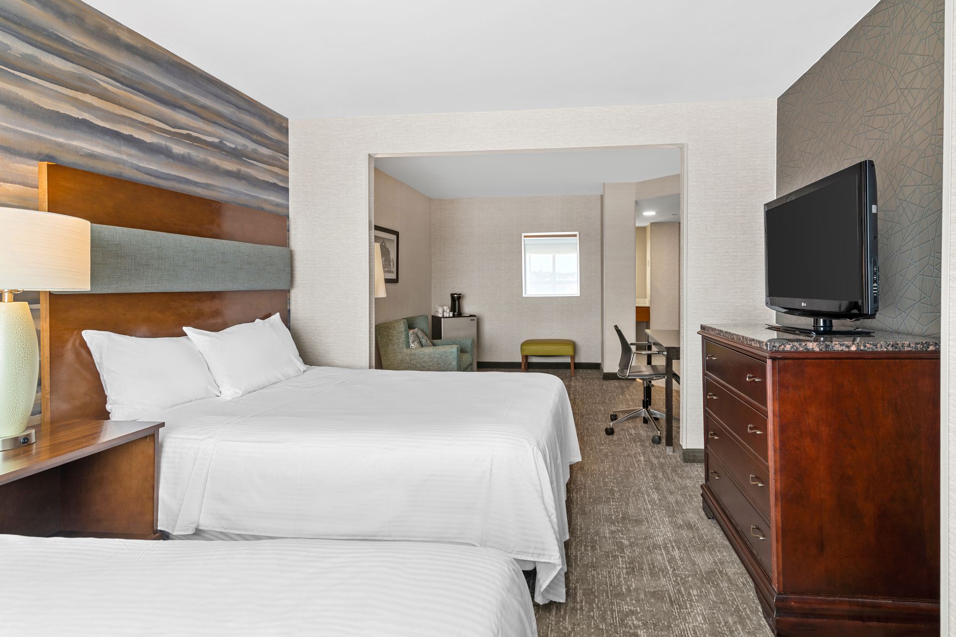 Hotel room with two beds, a dresser, TV, and a view into a sitting area