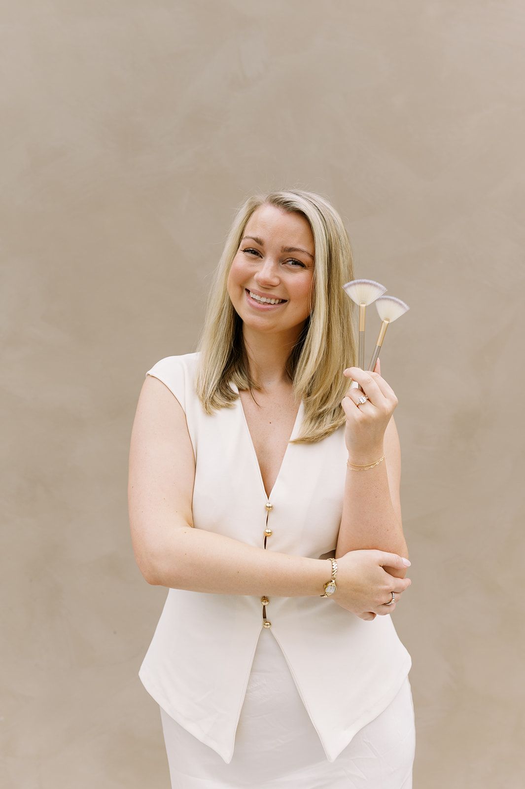 Smiling woman in white holding a facial brush against a beige background