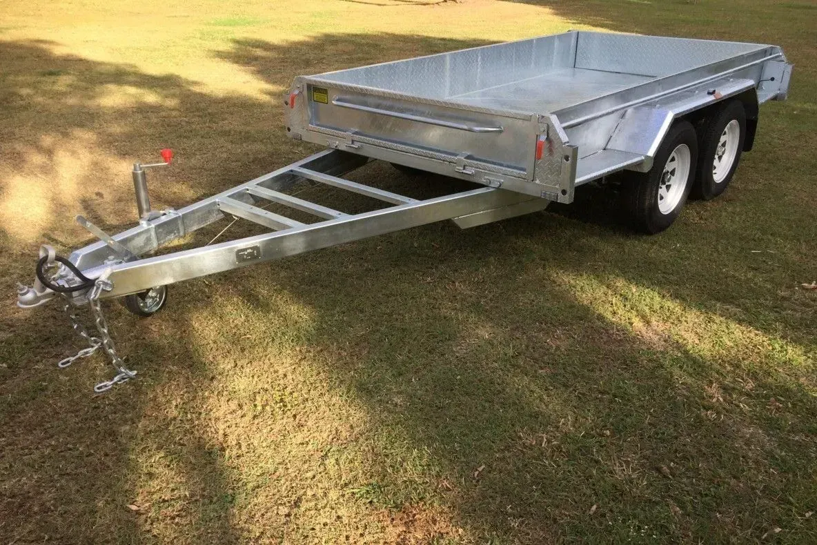Silver utility trailer with ramp and tandem wheels parked on grass outdoors
