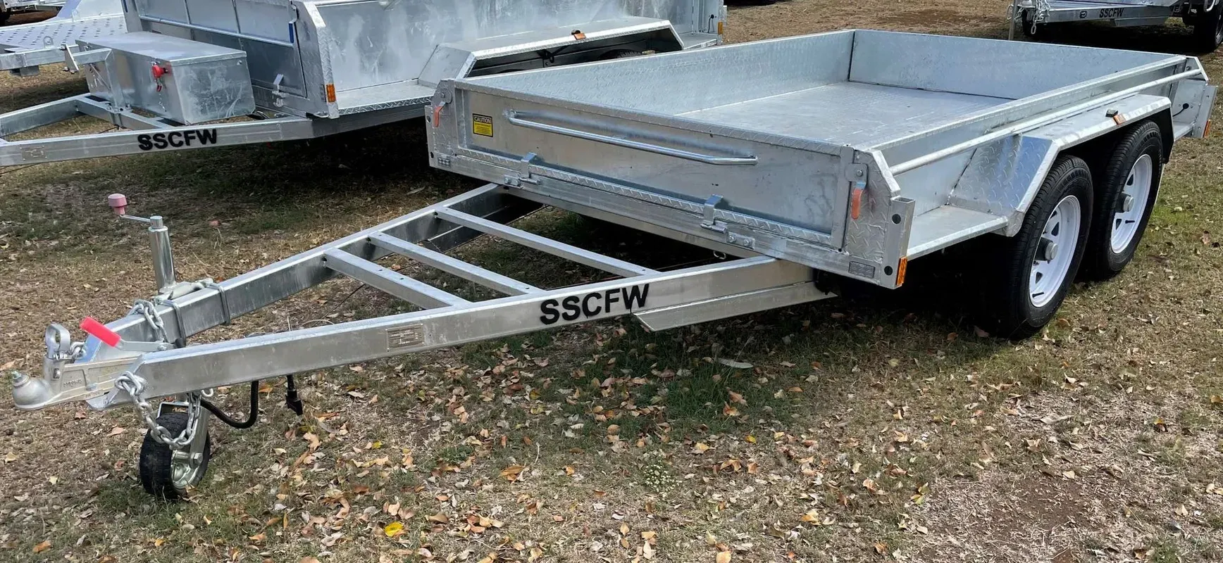 Silver Utility Trailer with Mesh Ramp Gate and Twin Axles Parked on Gravel Outside — SSCFW Trailers In Innisfail, QLD