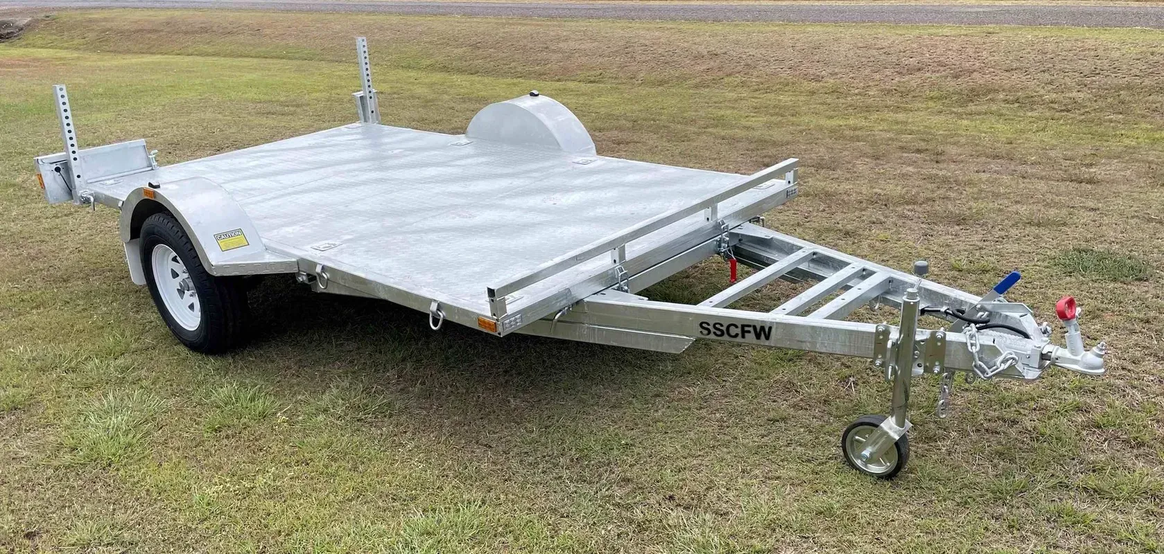 Silver Flatbed Utility Trailer on Grass, with A Hitch, Jack Wheel, and Single Visible Wheel — SSCFW Trailers In Mareeba, QLD