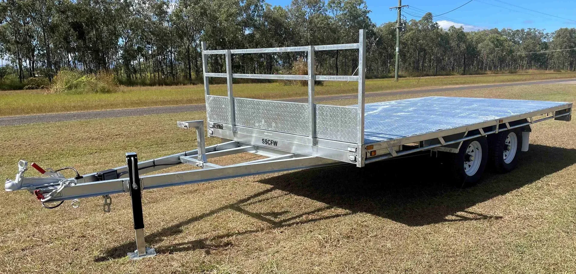 Silver Flatbed Utility Trailer with Railings and Hitch, Parked on Grass Under a Blue Sky — SSCFW Trailers In Cairns, QLD