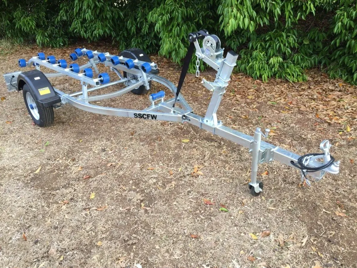 Grey Boat Trailer with Blue Rollers Parked on Dirt Beside Greenery — SSCFW Trailers In Mareeba, QLD