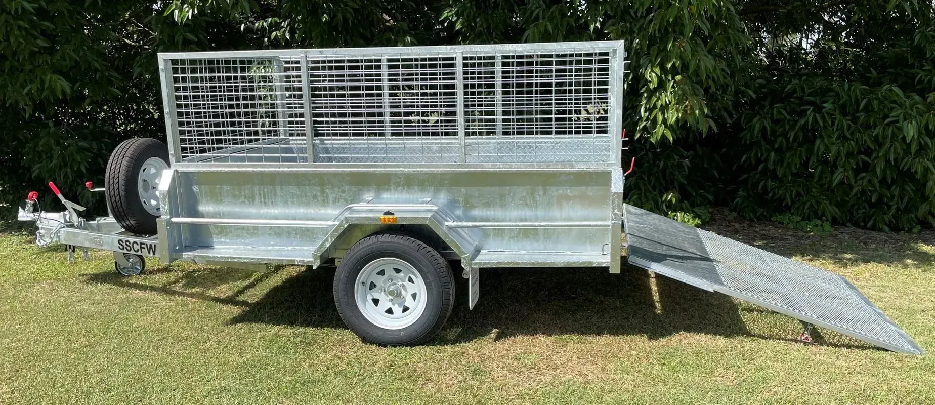 Silver Utility Trailer with Mesh Sides and Ramp, Parked on Grass Outdoors — SSCFW Trailers In Mareeba, QLD