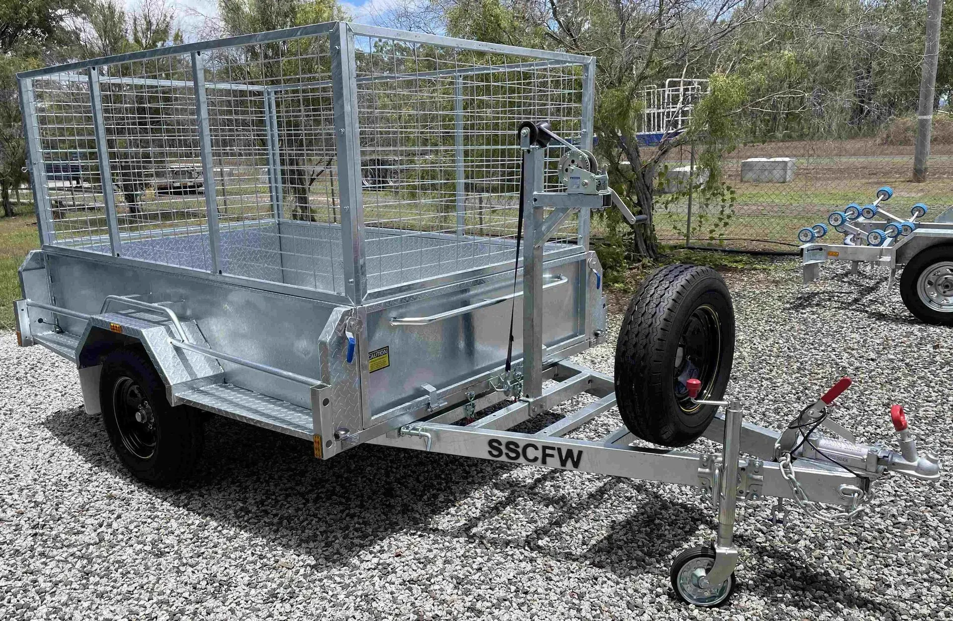 Galvanized Utility Trailer with Mesh Sides and Spare Tire, Parked on Gravel Outdoors — SSCFW Trailers In Mareeba, QLD