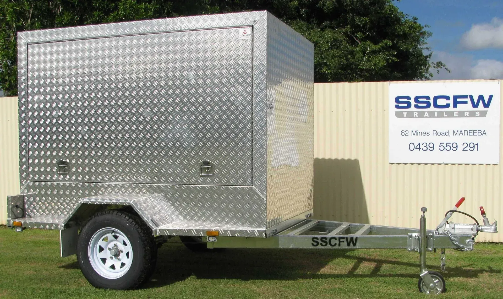 Silver Enclosed Cargo Trailer with SSCFW Logo Parked on Grass Beside a Building — SSCFW Trailers In Mareeba, QLD
