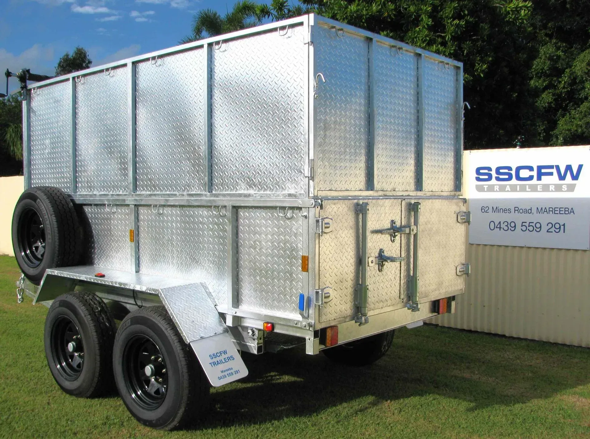 Silver Dual-Axle Trailer with A Front Door, Parked on Grass Beside a Fence and Sign — SSCFW Trailers In Innisfail, QLD
