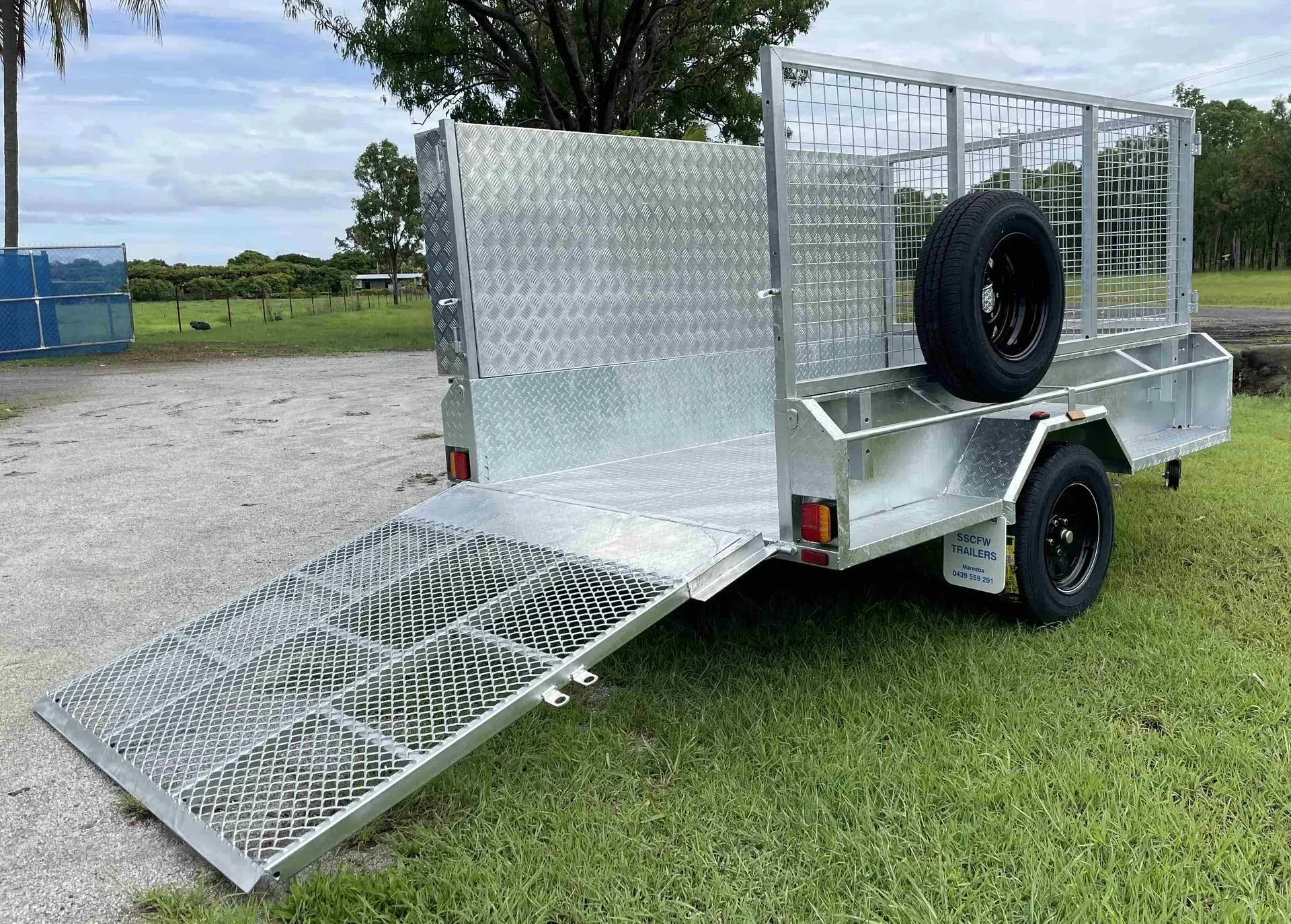 Silver Utility Trailer with Mesh Ramp Lowered on A Grassy Field — SSCFW Trailers In Cassowary Coast, QLD