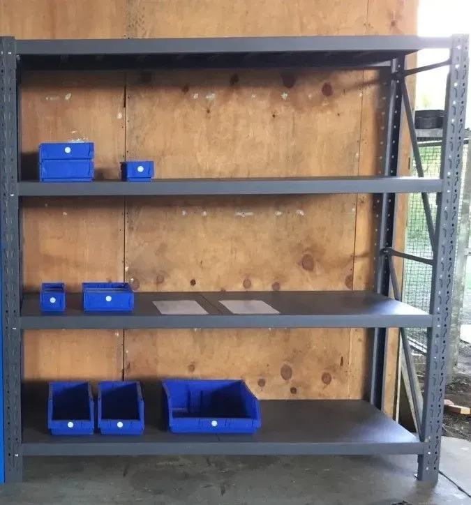 Empty Metal Shelving Unit with Blue Storage Bins Against a Plywood Wall — SSCFW Trailers In Innisfail, QLD
