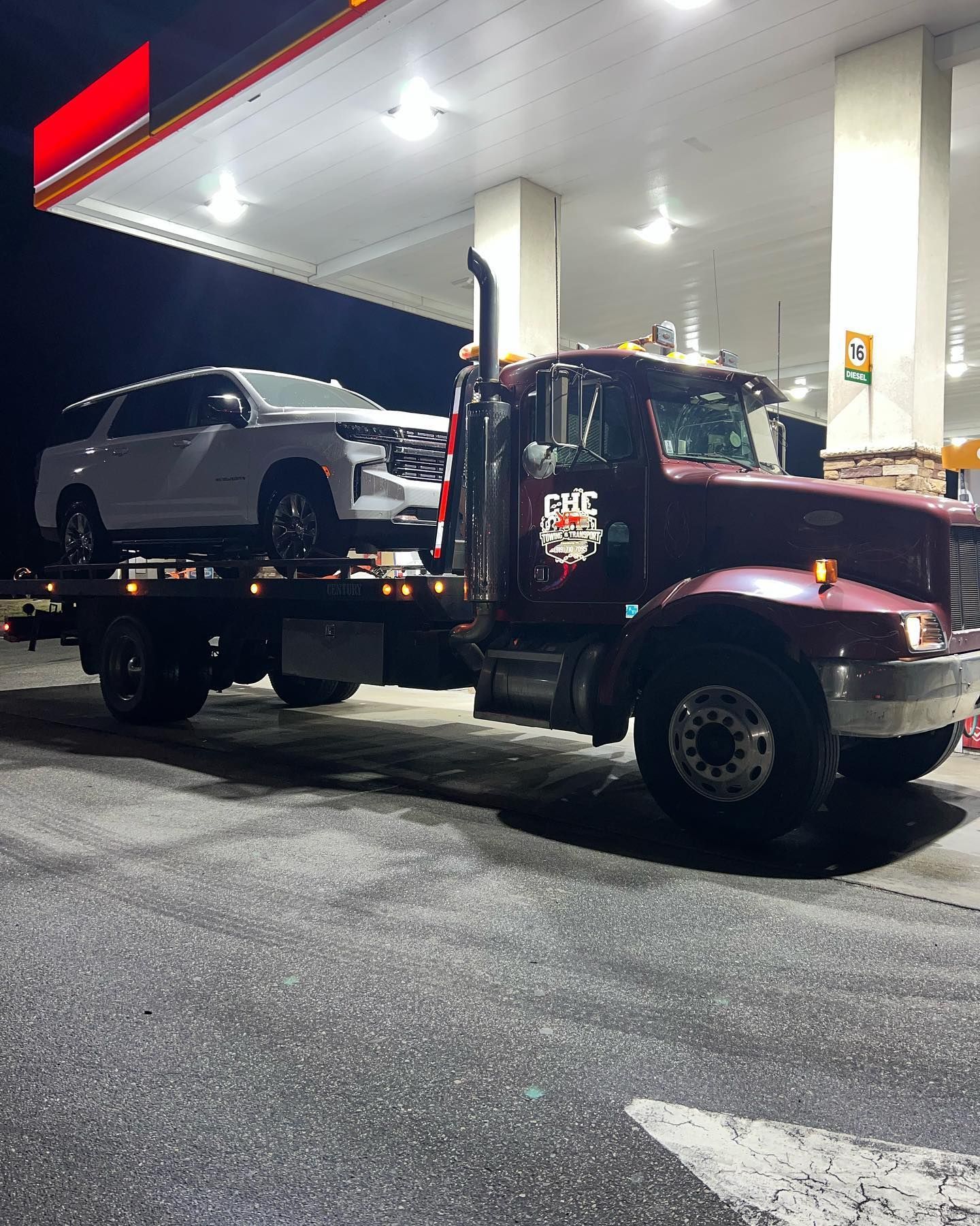 A tow truck with a car on the back is parked in front of a gas station.