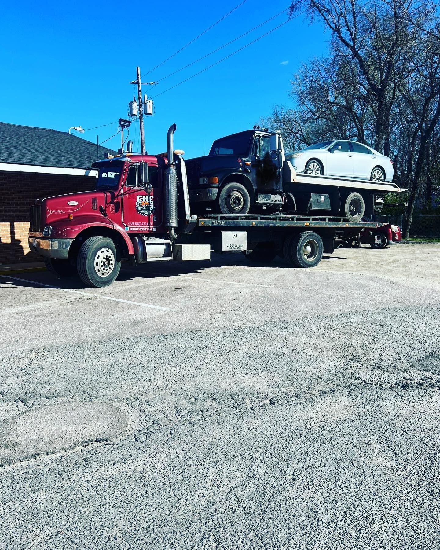 A red tow truck is carrying a black truck and a white car.