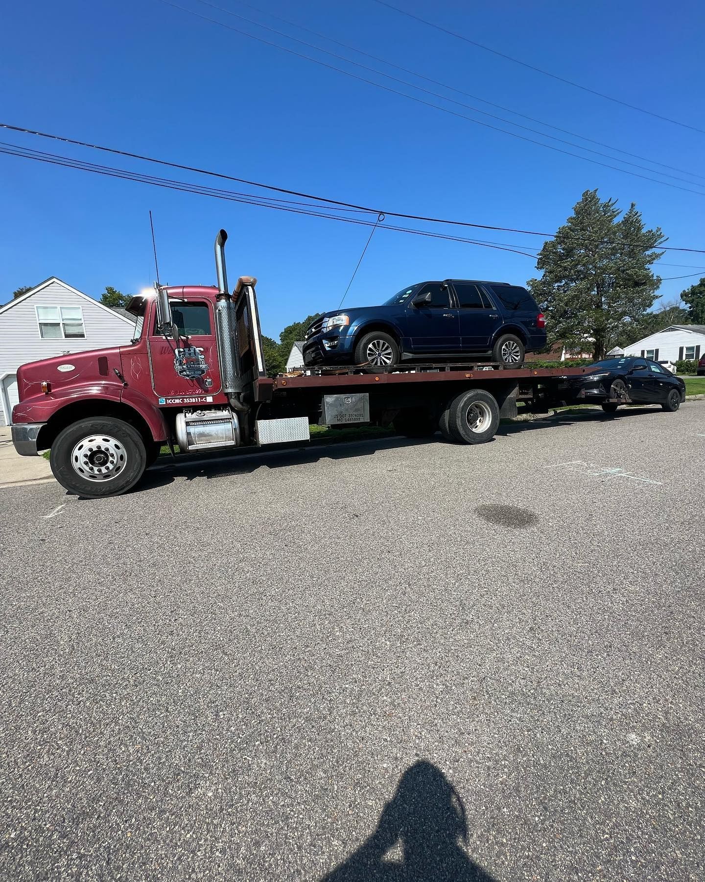 A red tow truck is towing a blue suv and a black car.