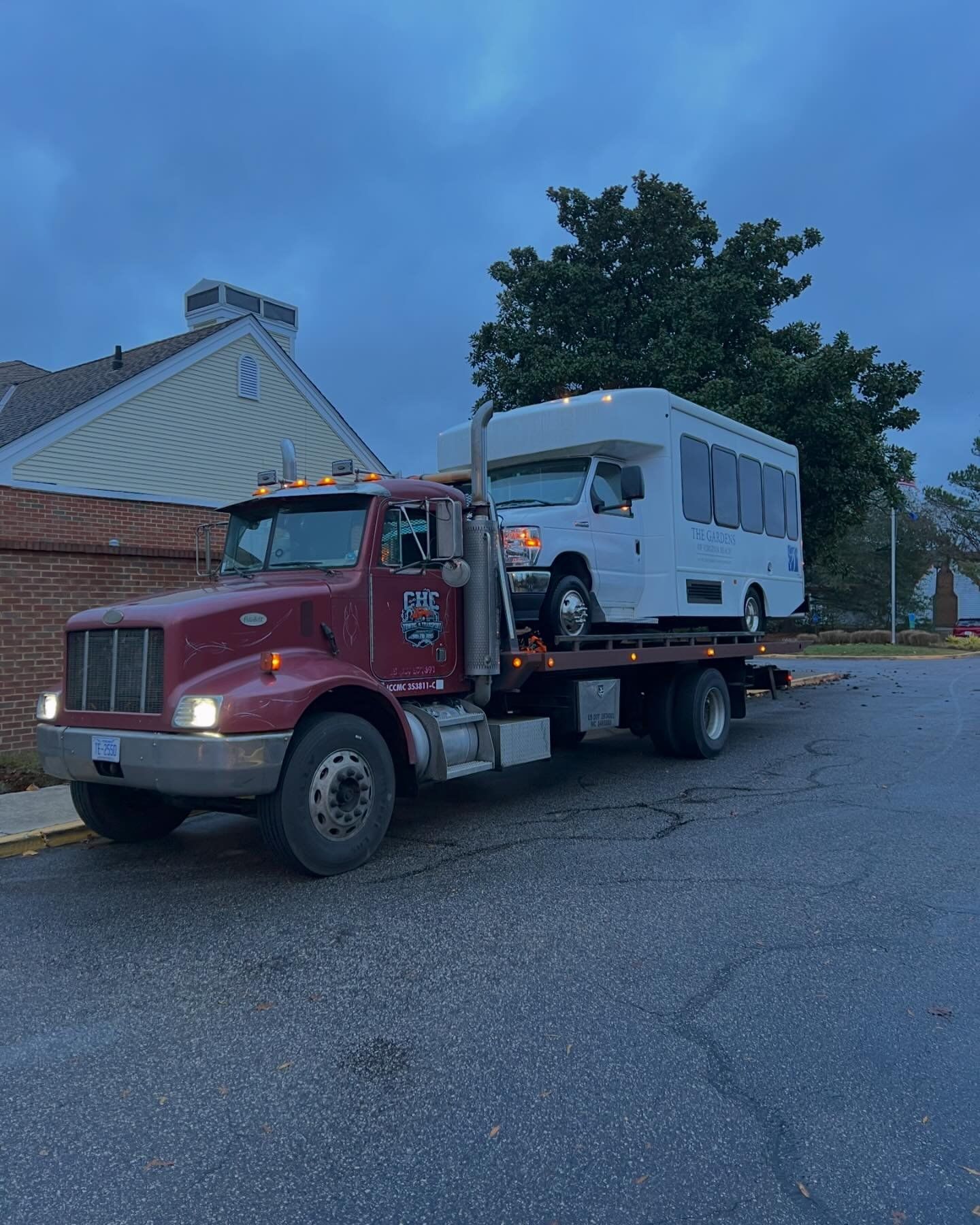 A red tow truck is carrying a white rv down a street