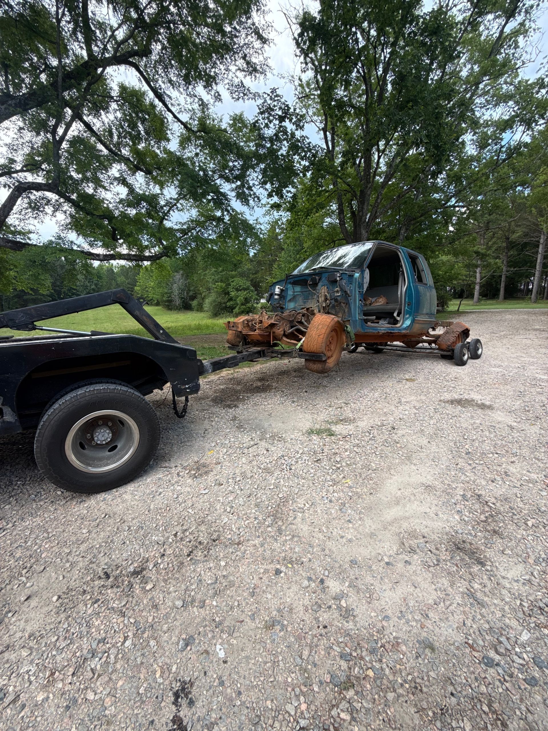Black truck towing a blue tarp-covered load on a gravel driveway under trees