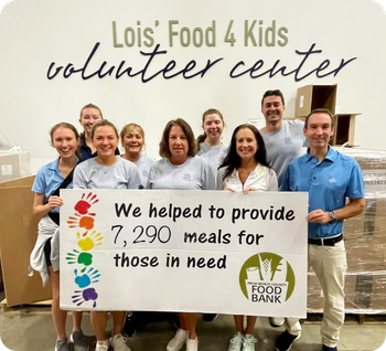 Volunteers hold a sign saying they provided 7,290 meals for Lois' Food 4 Kids in a warehouse.