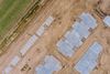 Aerial view of a construction site with blue tarp-covered foundations and dirt paths.