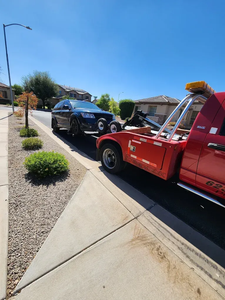 Tow truck towing a dark car on a residential street; bright sunny day.