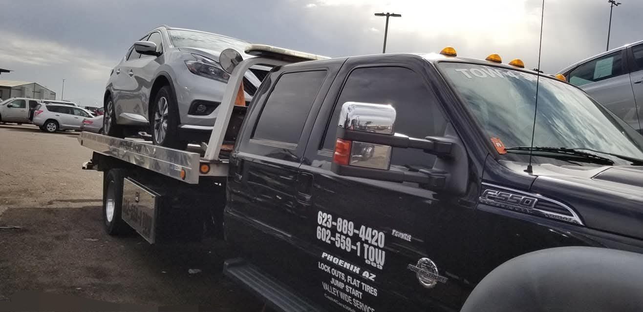 Black car being towed on a sunny day in front of a building with a