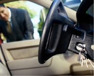 Man unlocking car door, keys in the ignition, focused on door, steering wheel in the foreground.