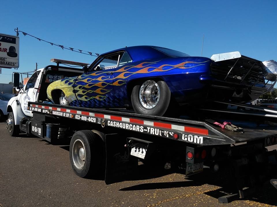 Blue custom car with flame design on a tow truck, outdoors.