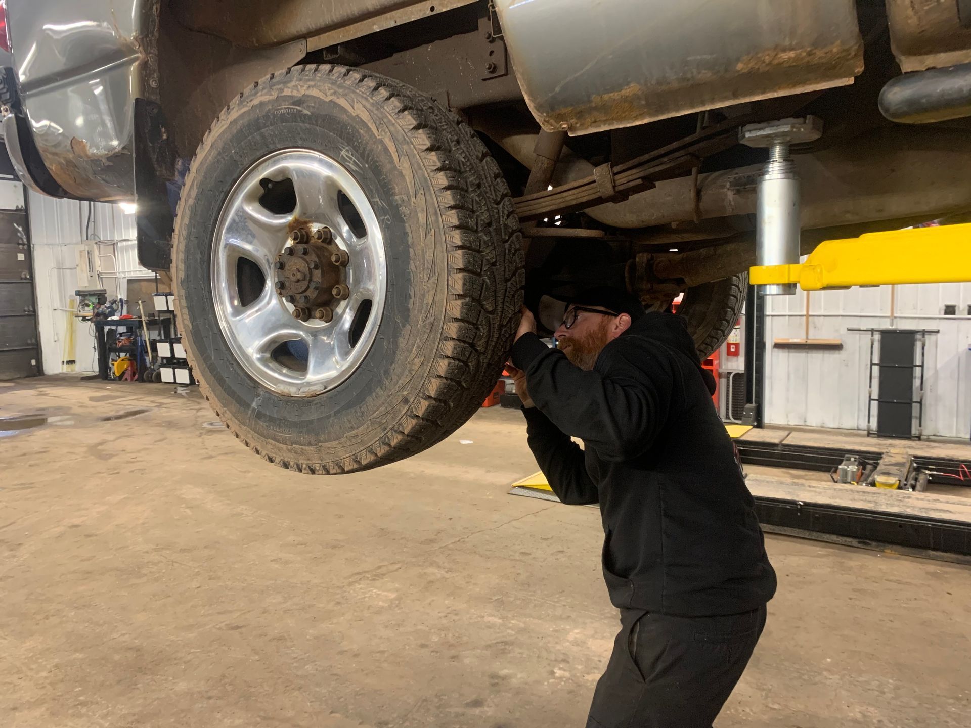 A man is working under a truck on a lift in a garage. | Tiny's Automotive