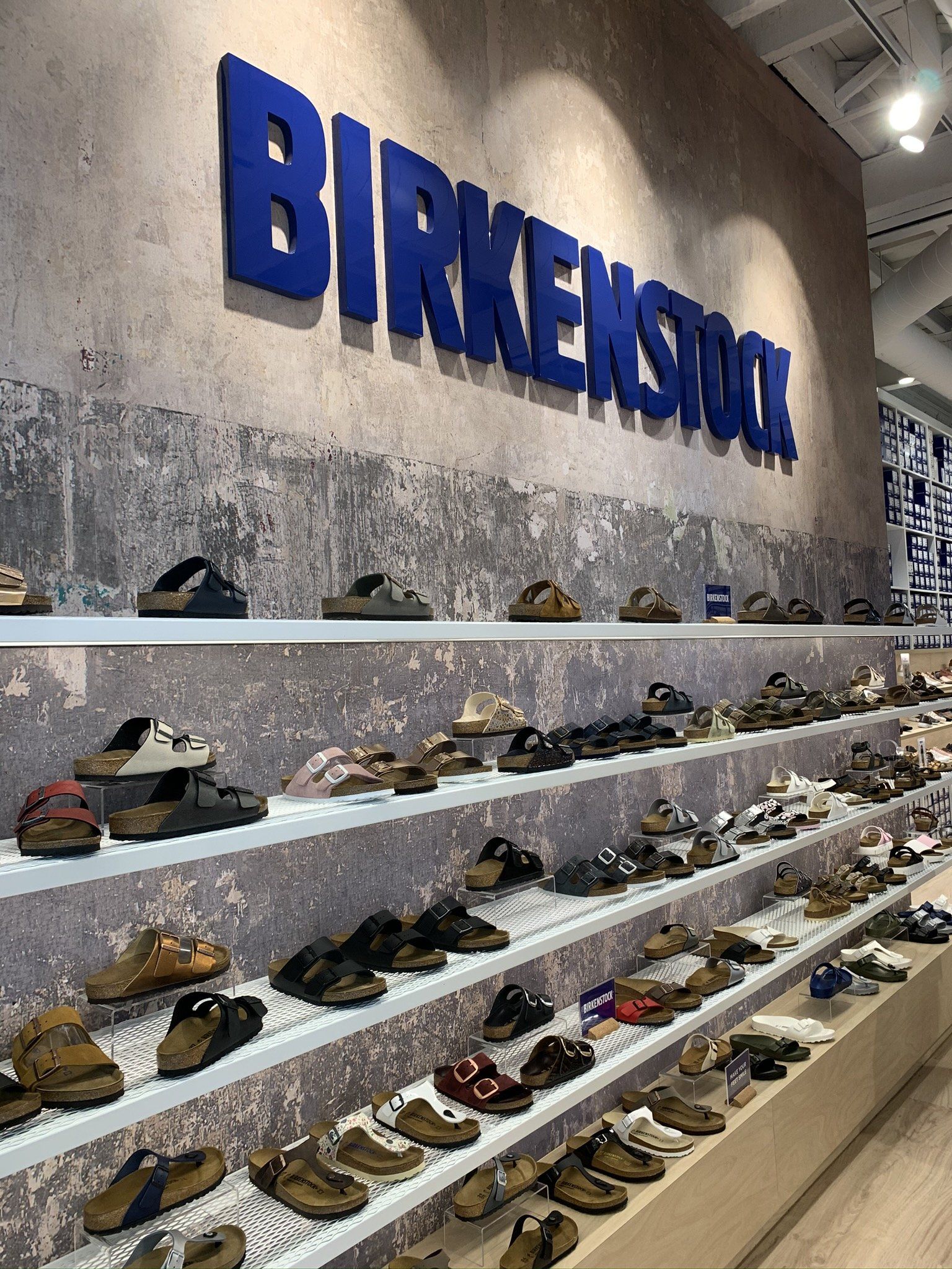 Birkenstock footwear display wall featuring a range of sandals and shoes arranged on shelves beneath large Birkenstock branding.